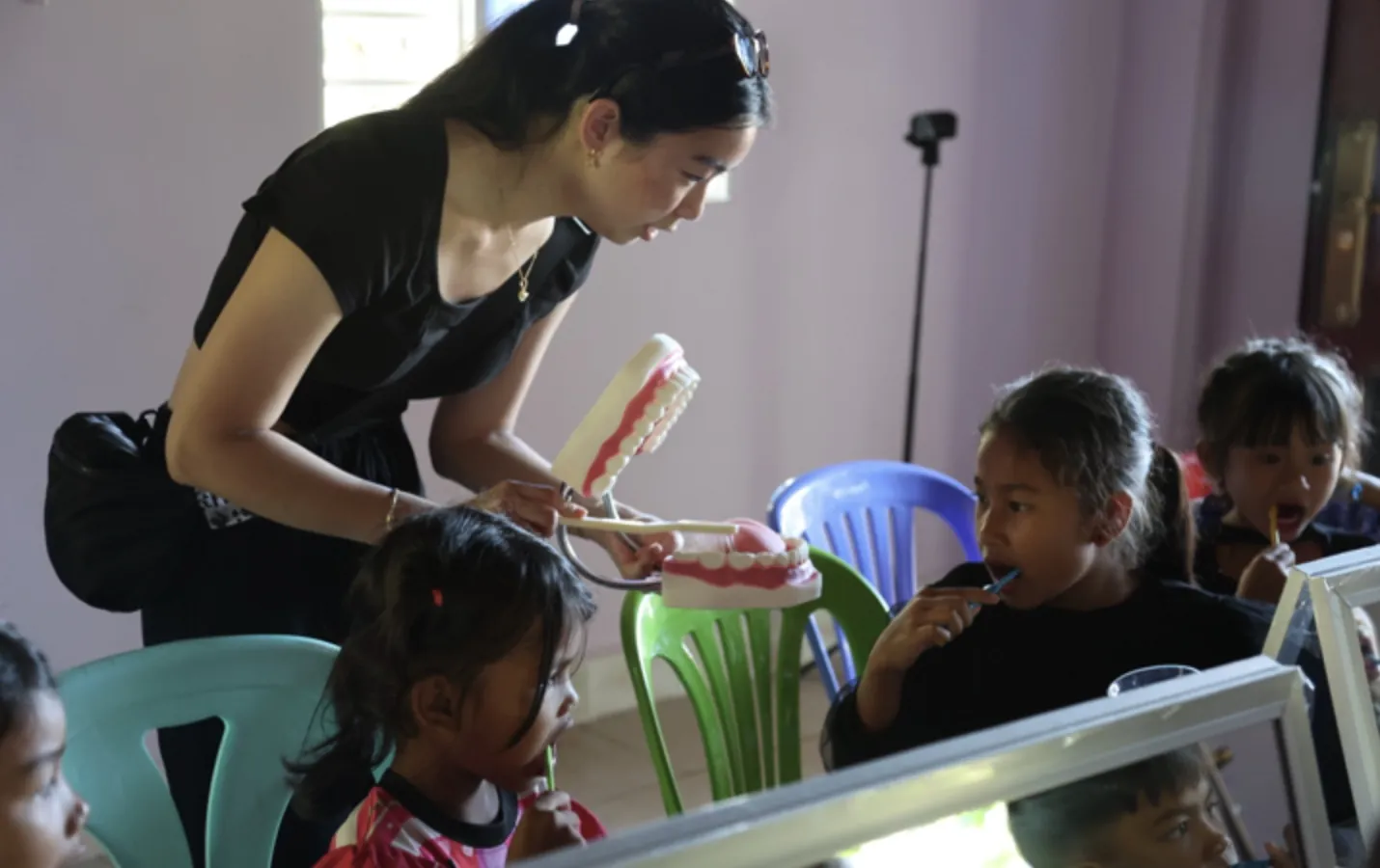 A volunteer teaching children to brush their teeth with a model of teeth