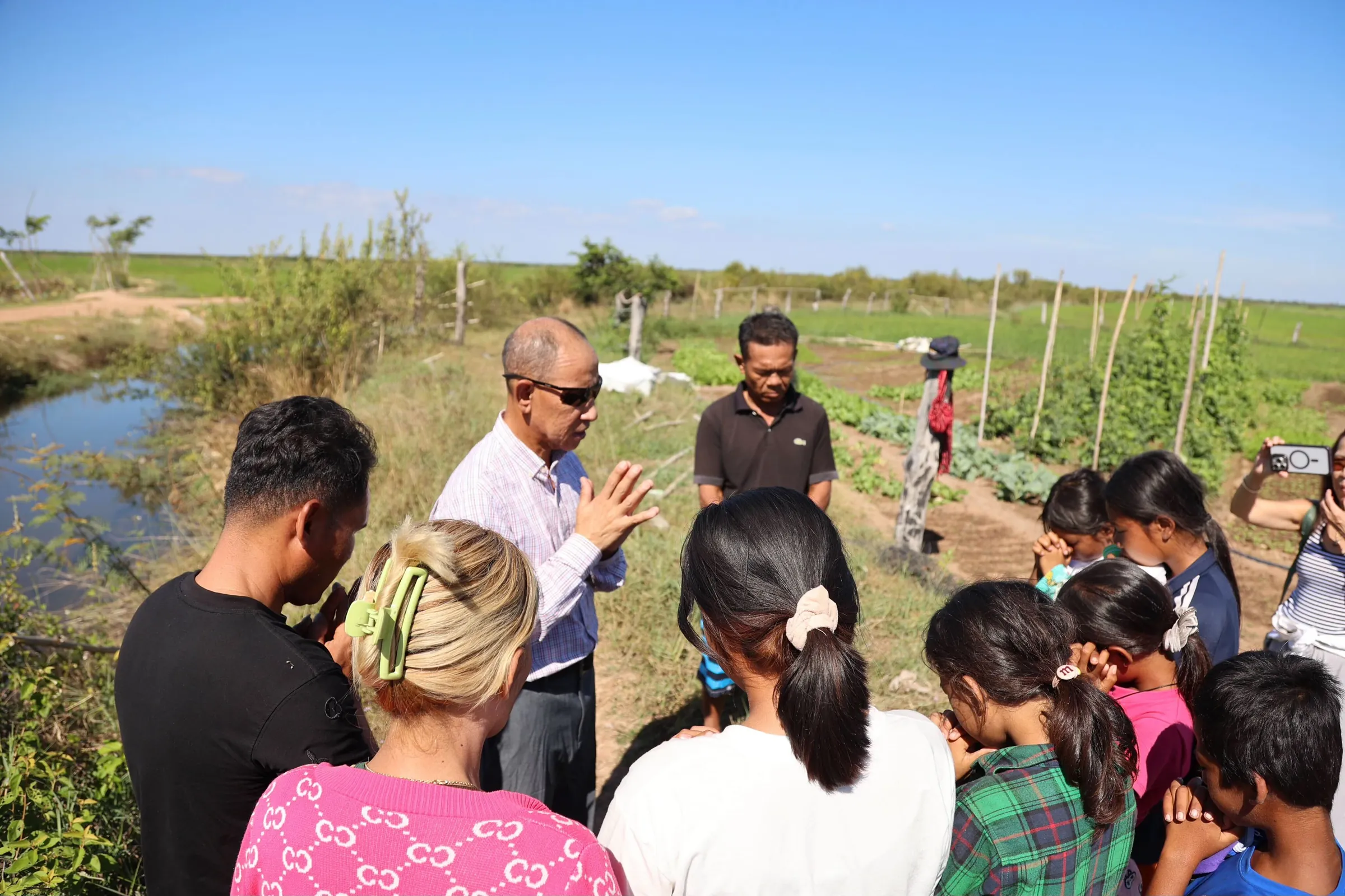 Rev. Peter Im leading a group of children and volunteers in prayer beside the garden at the Children's Center